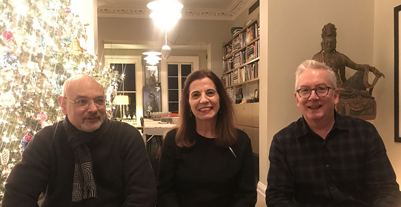 A photo of three persons sitting near a bright Christmas tree.