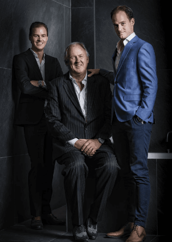Man in a sweater smiling with arms crossed while standing by a wooden wall.