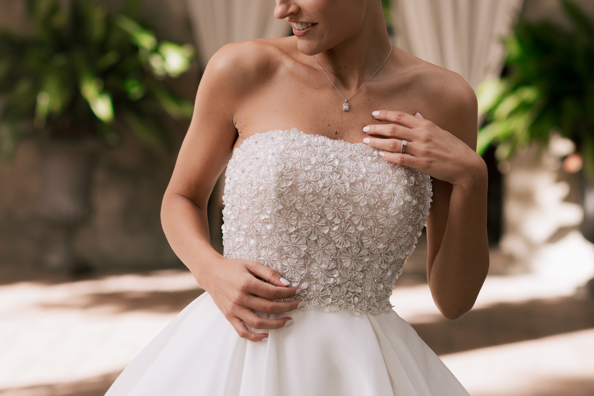 Sposa in abito bianco con corpetto beige ricamato, ritratto dai fianchi in giardino soleggiato di Villa Ferrari