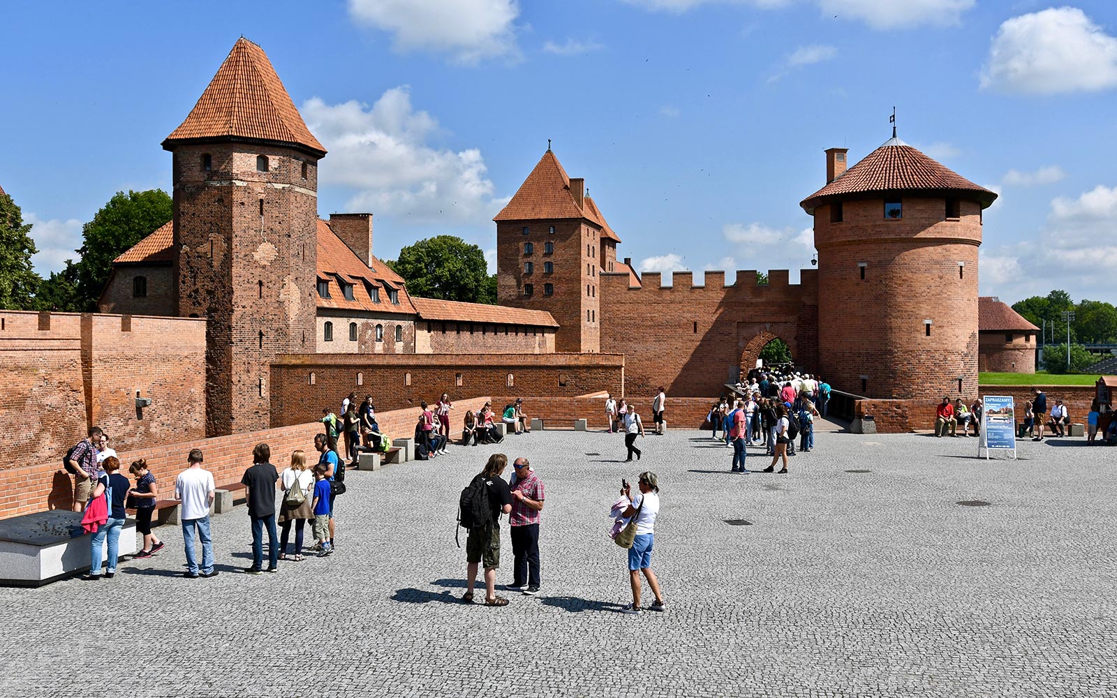 Odwiedzający zwiedzają dziedziniec zamku Malbork podczas wycieczki z przewodnikiem audio z Gdańska.