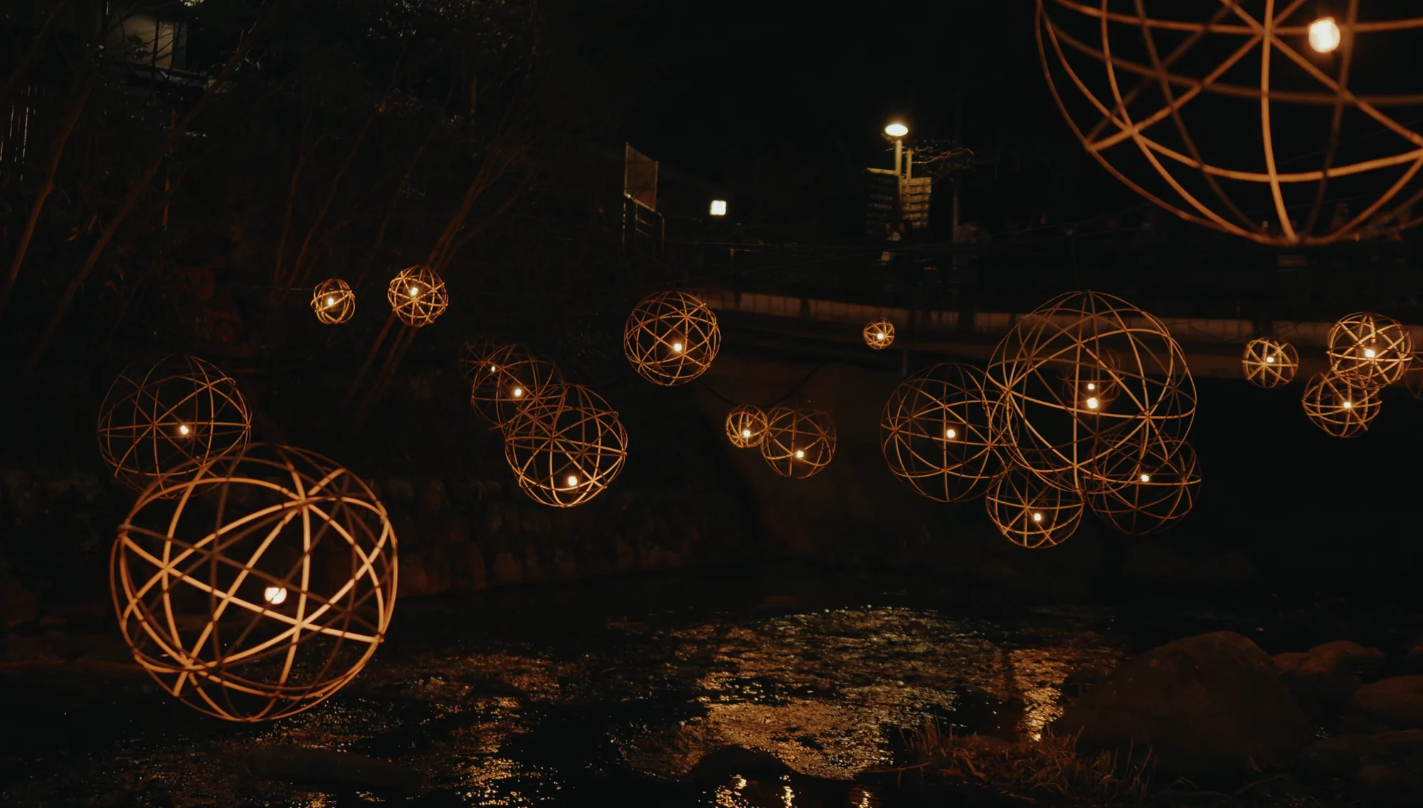 Woven bamboo lantern spheres glowing above dark water during Yuakari