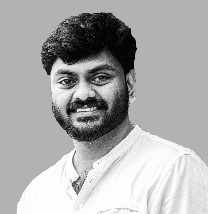 Person wearing a blue puffer jacket and red backpack standing in front of a light blue building on a city street.