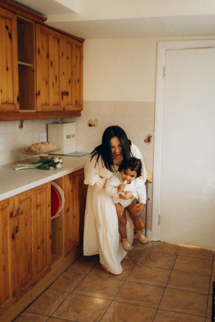 Woman with a toddle in white dress playing in a kitchen setting