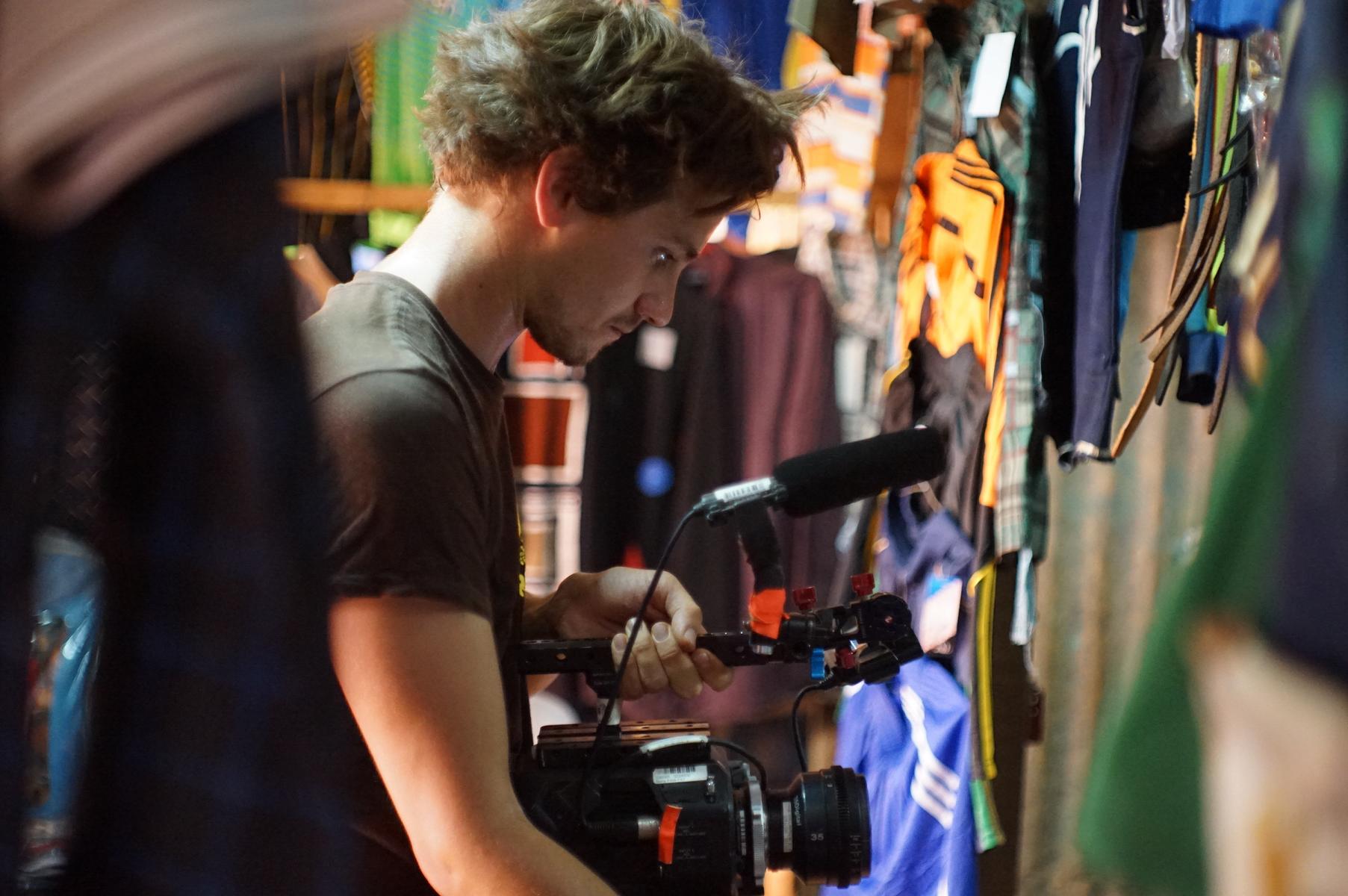 A man with short dark hair and a trimmed beard, wearing a blue shirt, sits in front of blue lockers and looks at the camera.