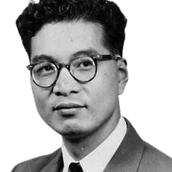 A black-and-white portrait of a young man wearing round glasses, a suit, and a tie, likely from the mid-20th century. He has short, neatly styled curly hair and an expression that is both composed and thoughtful, giving the image a vintage and professional look.