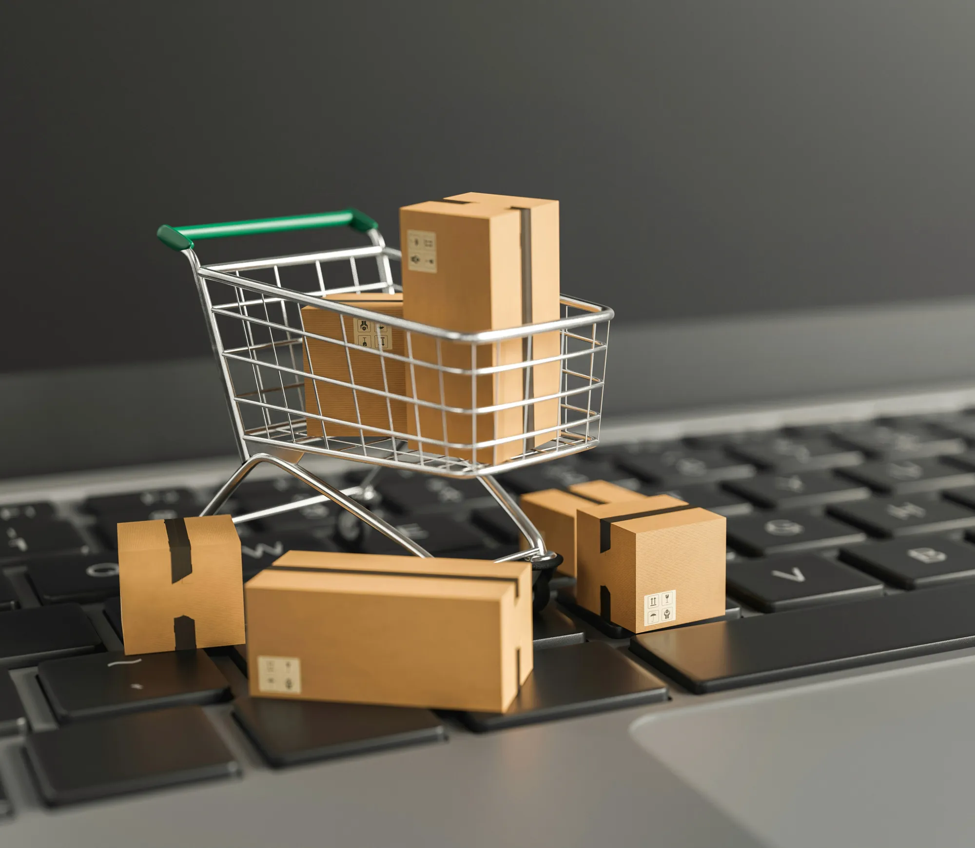 A miniature shopping cart filled with cardboard boxes on a laptop keyboard