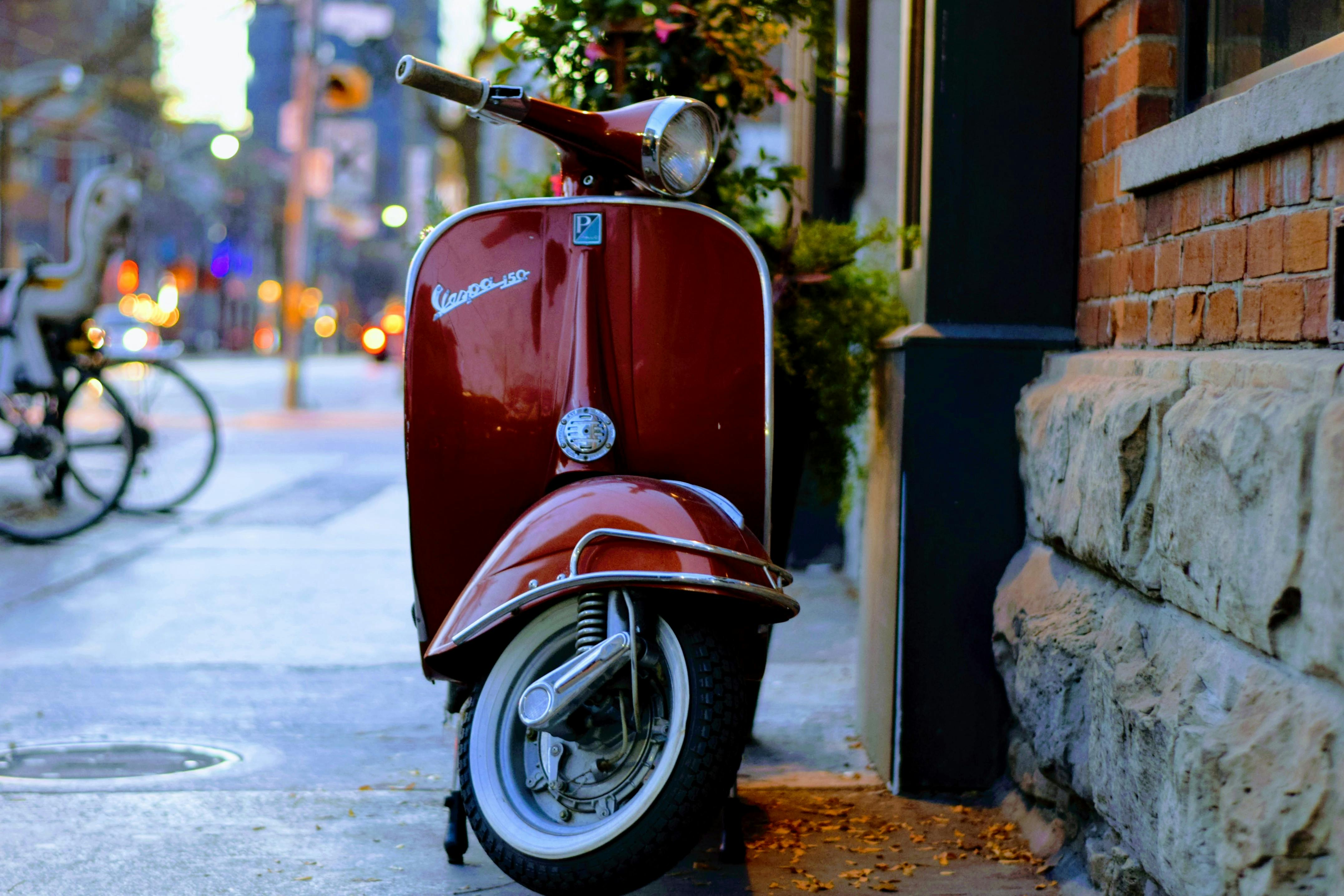 Vespa rossa parcheggiata lungo una via cittadina al tramonto, icona italiana di movimento, indipendenza e libertà di scegliere la propria direzione.