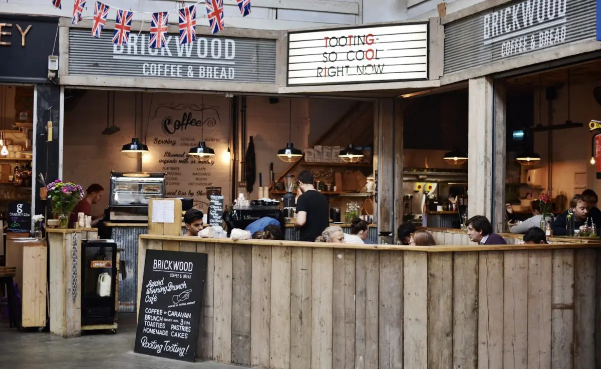 Modern house with angular design features a large pool and sun loungers on a wooden deck. Glass walls show a cozy interior. Sunset sky in the background.