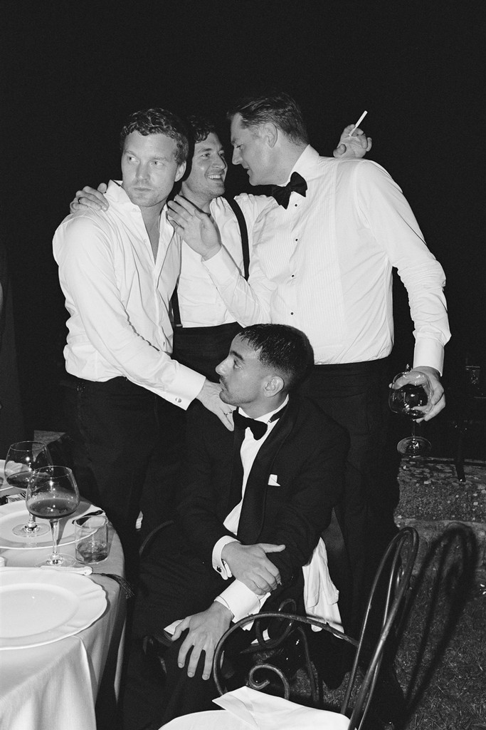 Black-and-white candid of groom and his friends, laughing and holding a glass of wine