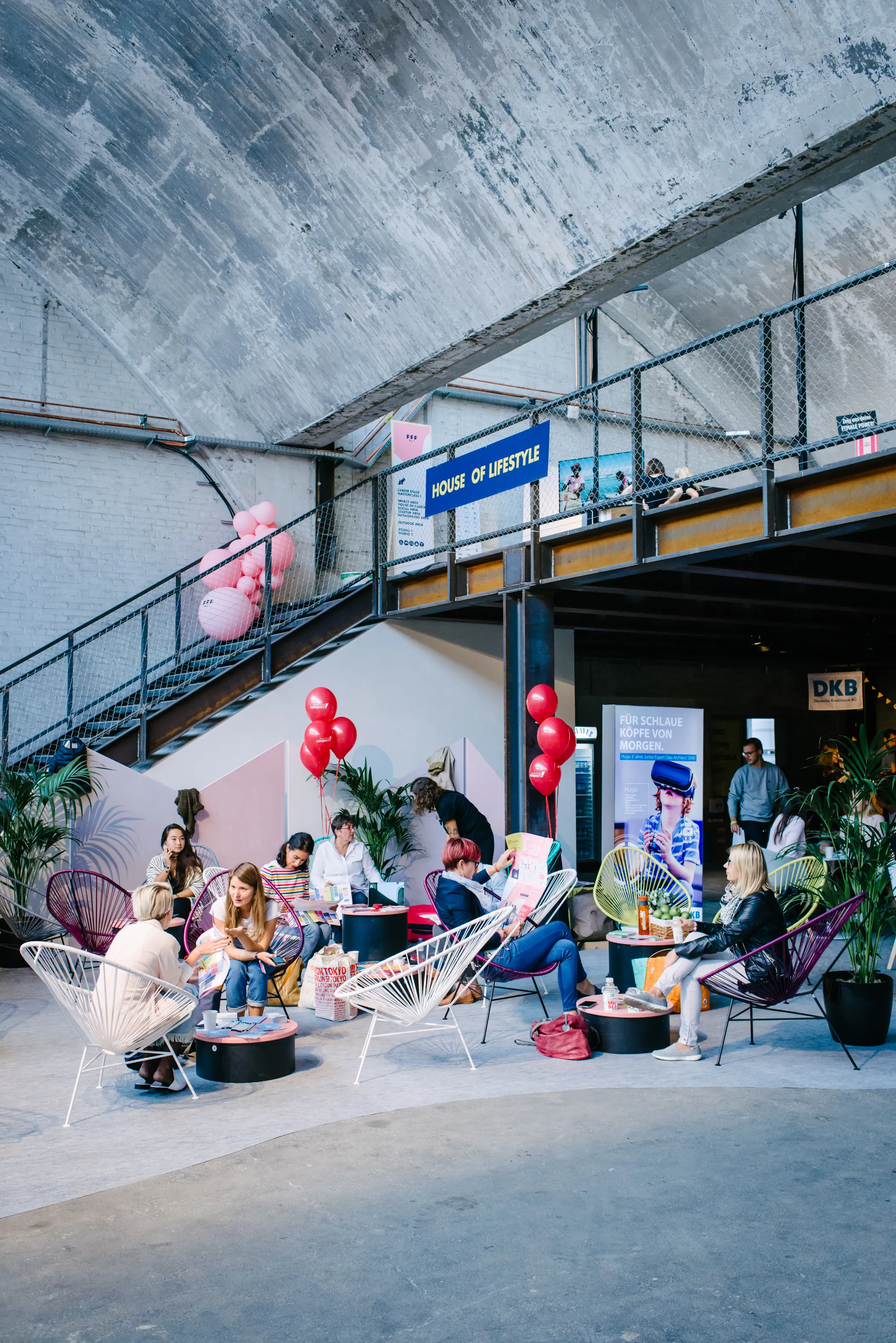 Lounge corner at the FEMALE FUTURE FORCE DAY with white and burgundy wire chairs, pink and red balloons and a House of Lifestyle sign under a concrete arch.