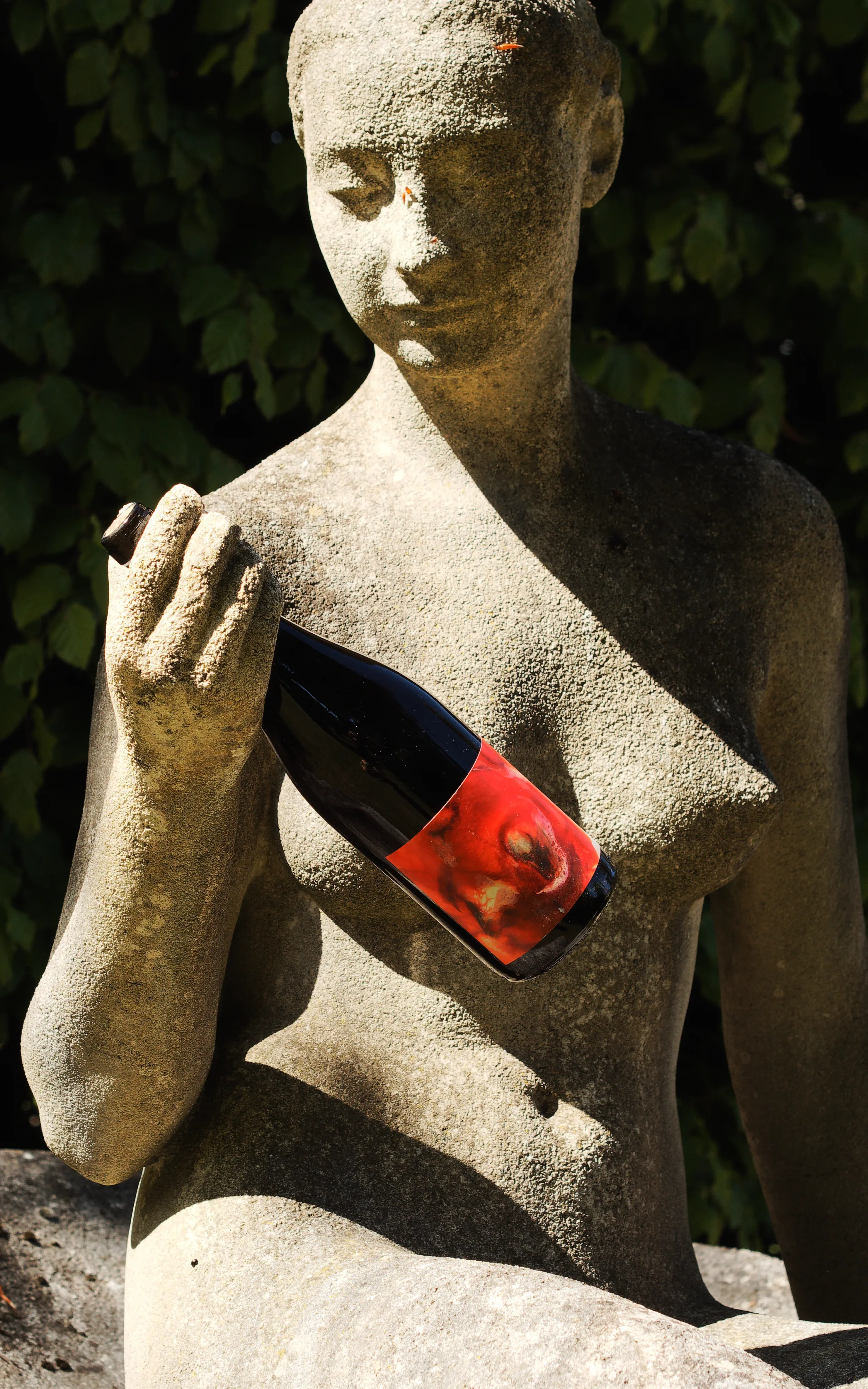 Photo produit d'une bouteille de vin nature tenue par une statue ensoleillée