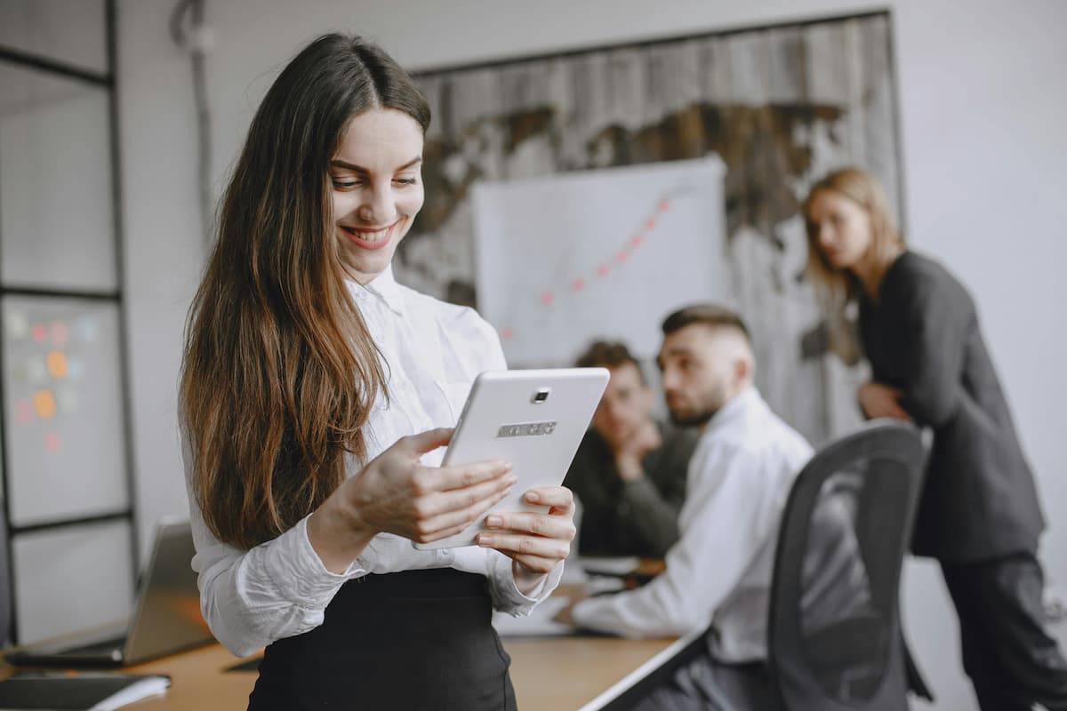 Mulher usando tablet em ambiente corporativo enquanto equipe trabalha ao fundo, representando a análise de oportunidades e os diferentes tipos de franquia no mercado.