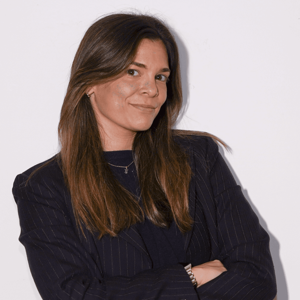 Professional portrait of a woman in a gray blazer and black turtleneck, smiling warmly against a light background.