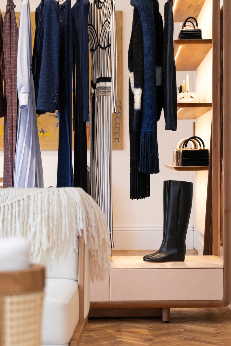 A boutique display featuring clothing, accessories, and black leather boots on wooden shelves with warm lighting.