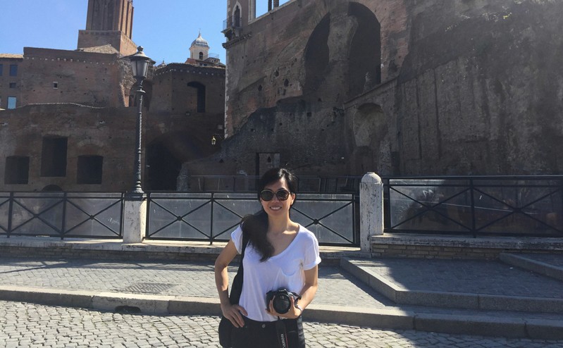 woman with glasses holding camera in front of ruins