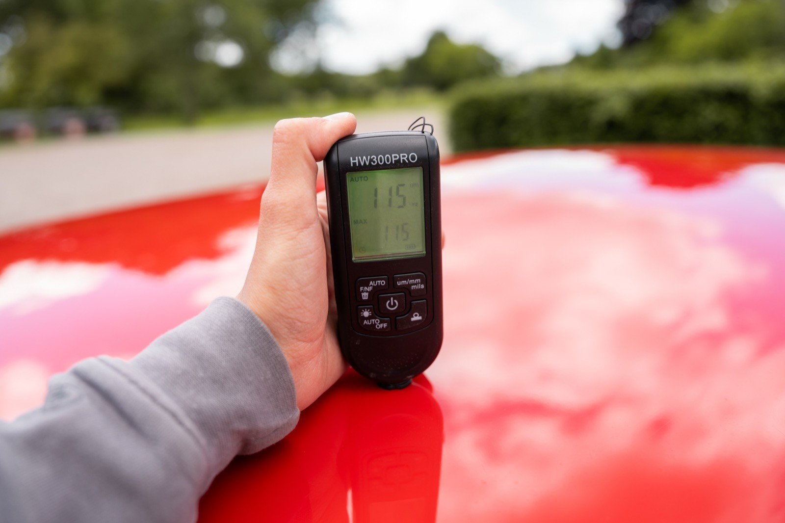 A hand holds a digital device displaying a screen, resting on a shiny red surface with greenery in the background.