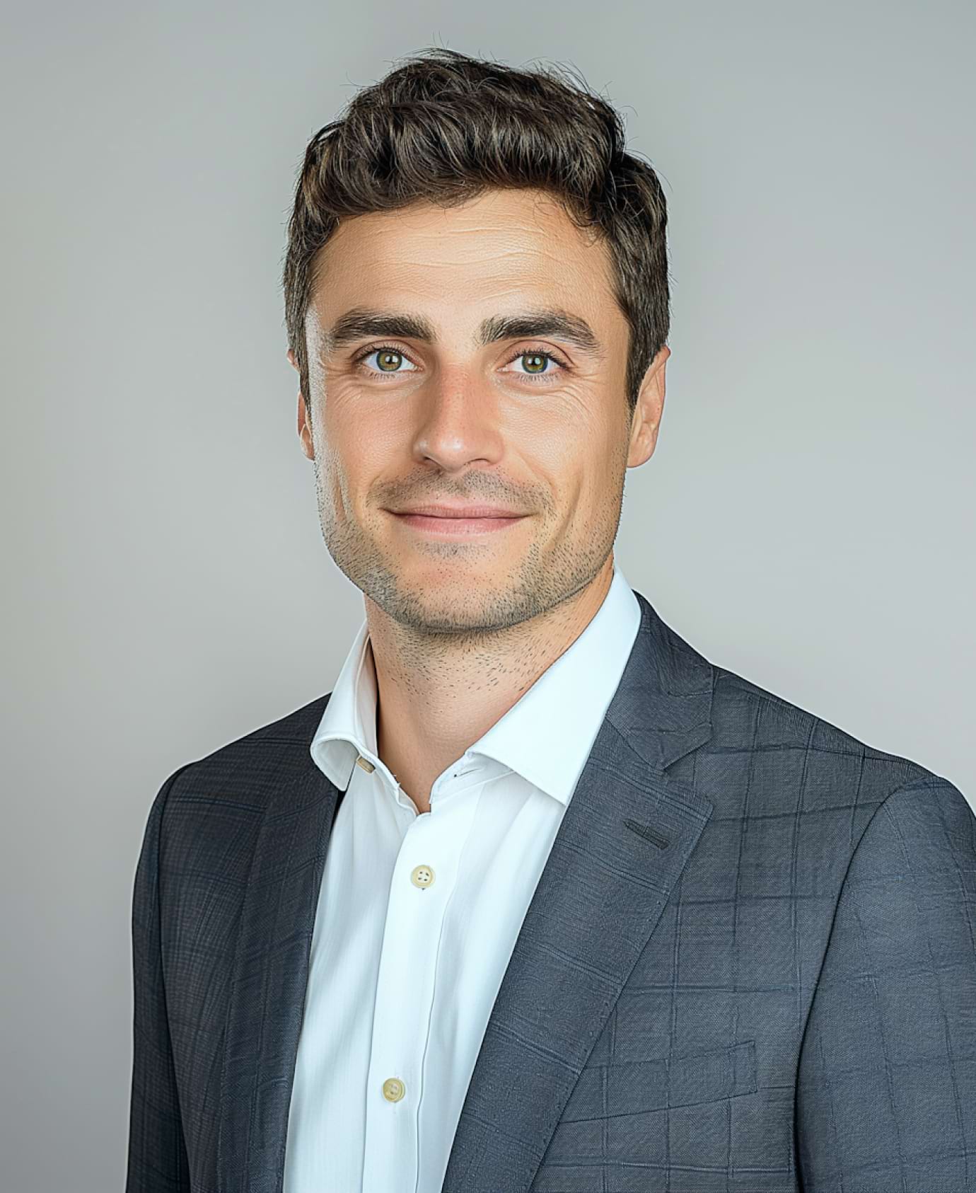 A man in a checkered grey suit and white shirt smiles slightly against a plain grey background, conveying a professional and approachable tone.