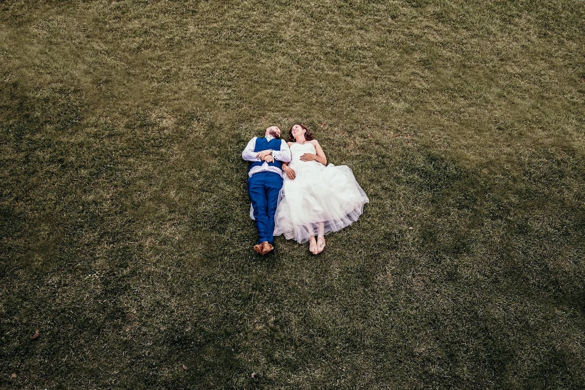 Bride and groom lying on grass captured from above on their wedding day