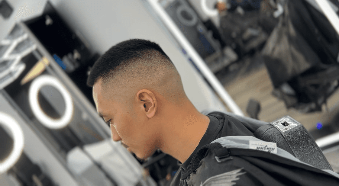 Man with short curly hair and a low fade on the sides, sitting in a barbershop chair.