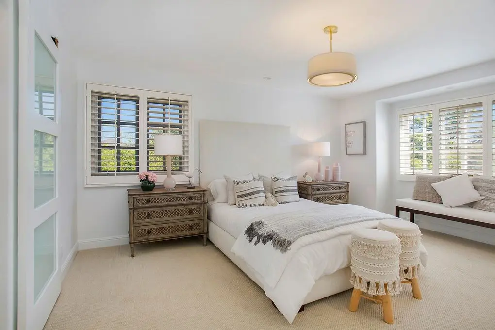 'Port Streets Remodel' bedroom with plush bedding, textured nightstand, chic lighting, and a cozy window seat.