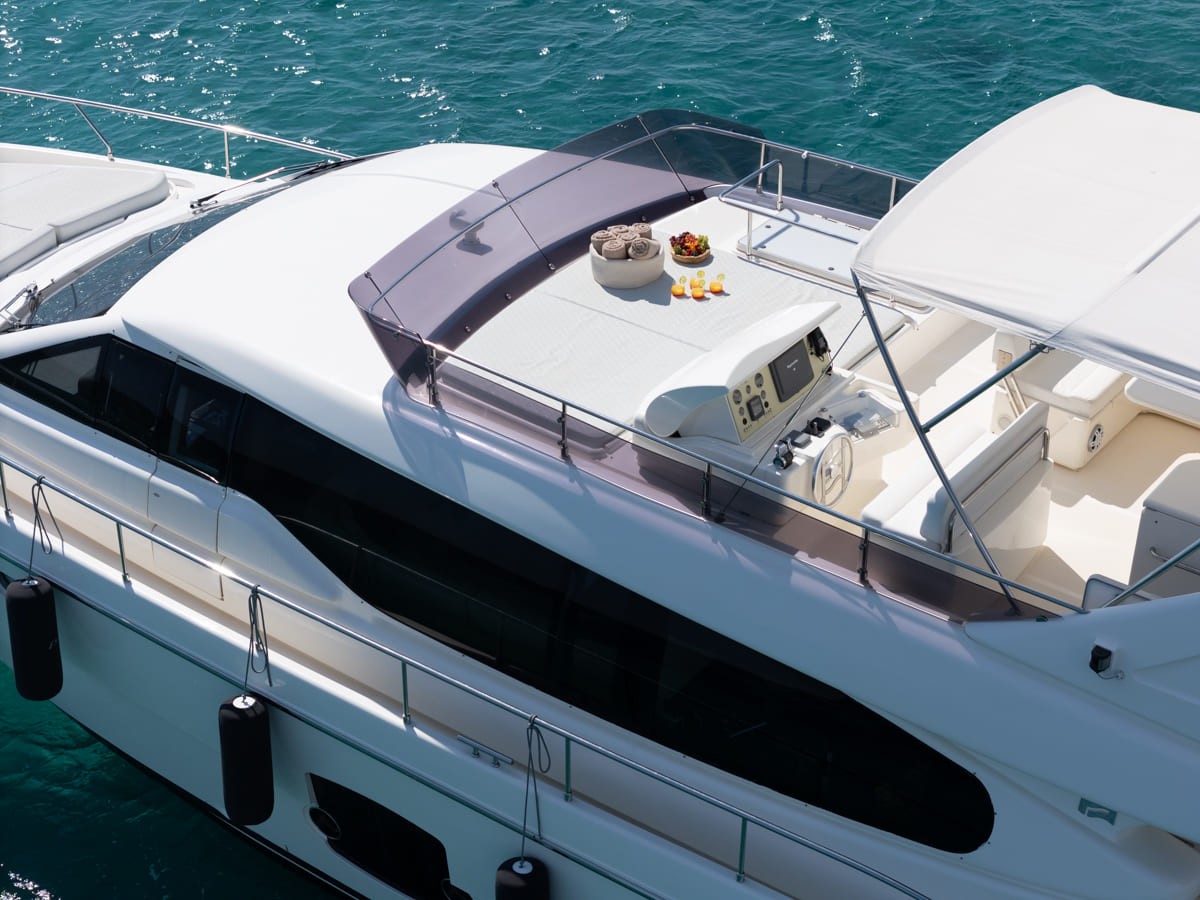 Modern white Ferretti 63 yacht with spacious flybridge featuring dining table set with appetizers, anchored in turquoise Aegean waters.