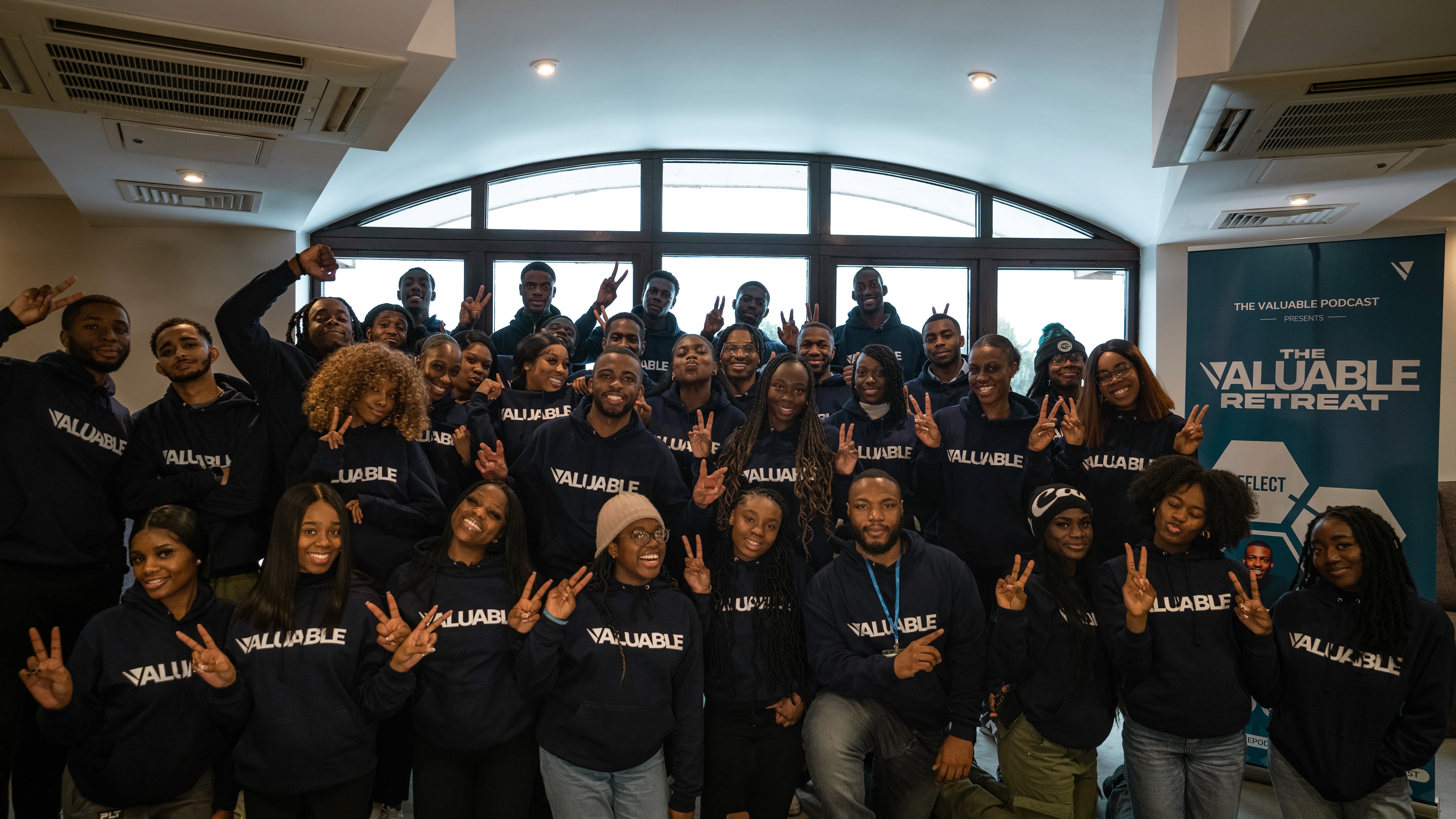 Indoor photo of large group of community members in navy Valuable sweatshirts, smiling together.
