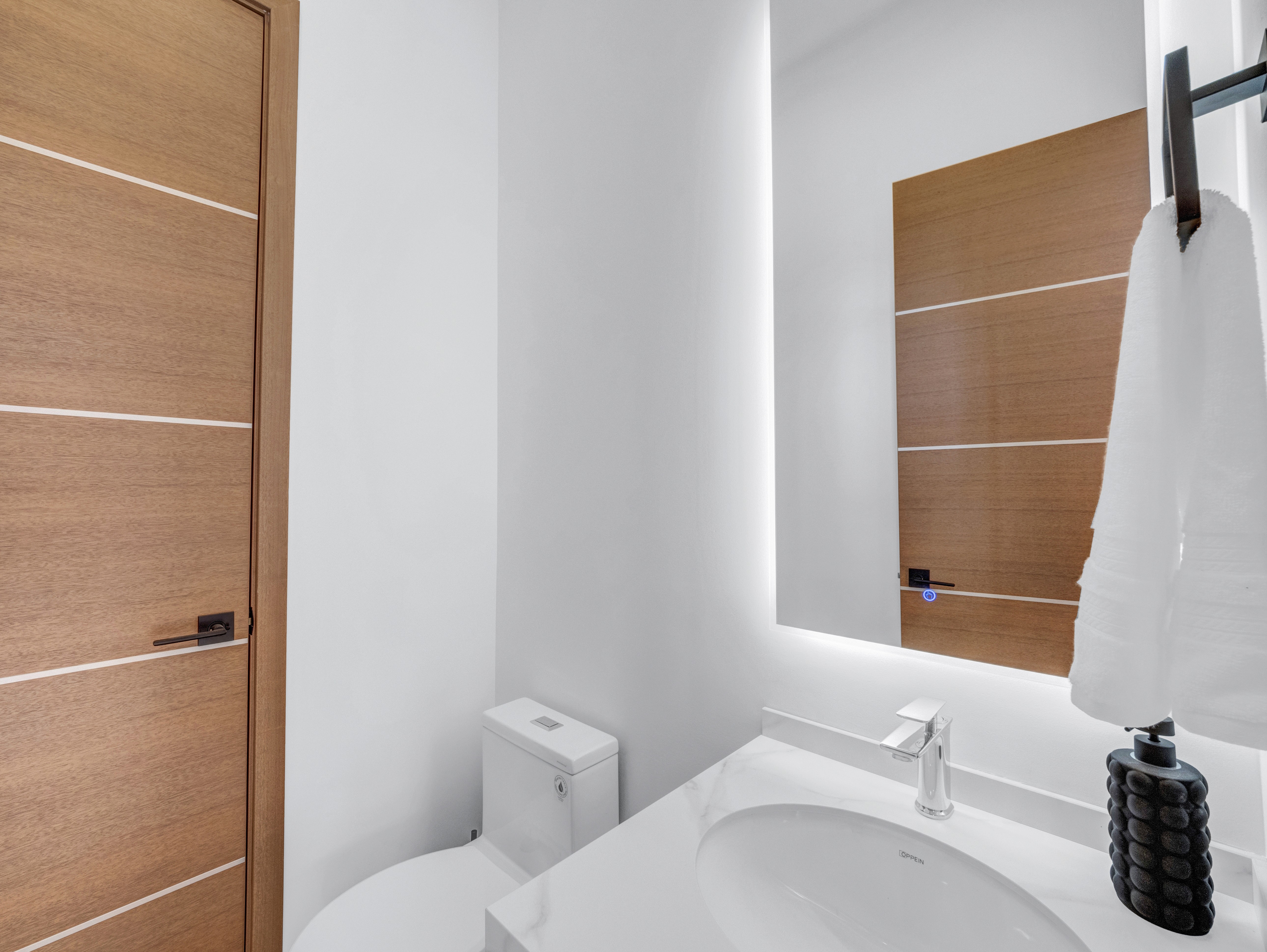 Minimalist powder room with a backlit mirror, marble sink, and warm wood accents