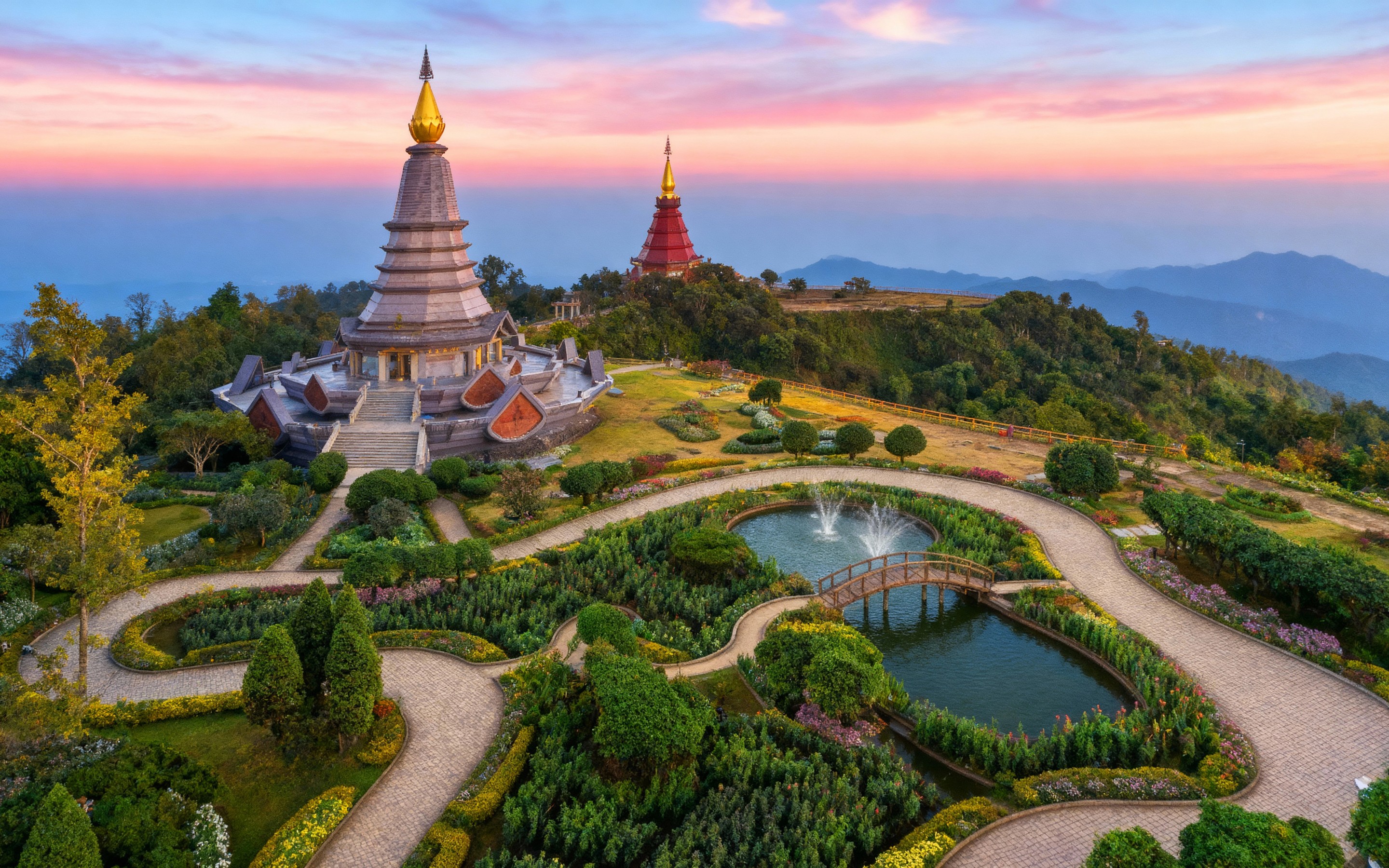 Aerial view of the twin pagodas of Doi Inthanon at sunrise, surrounded by lush gardens, fountains, and mountain scenery, capturing the serene beauty and spiritual essence of Chiang Mai, Thailand.