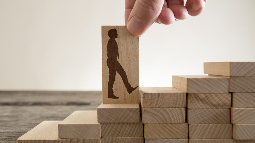 Man holding with his fingers wooden domino with shape of business man walking up