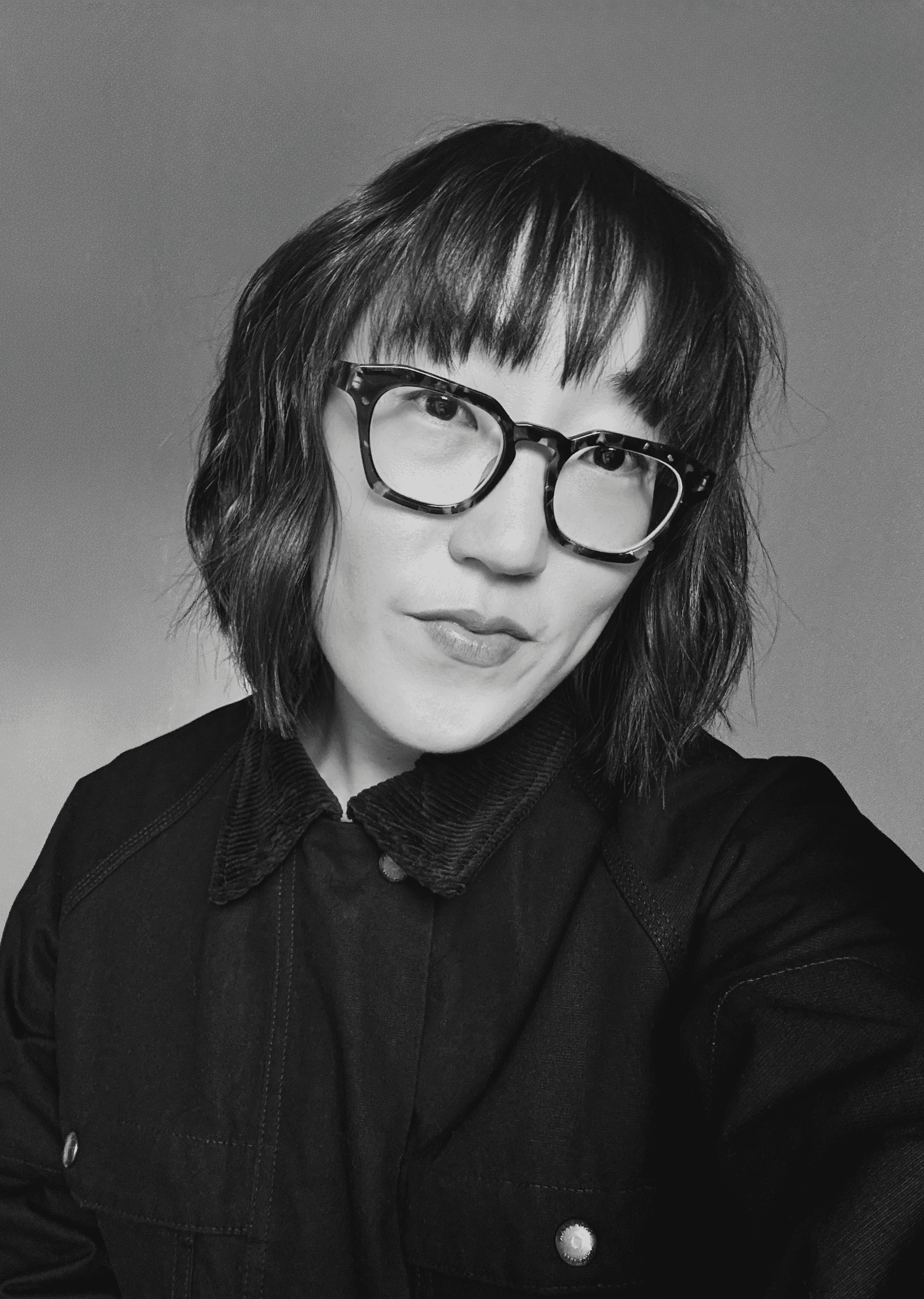 Sojin Rank, a Korean woman with short brown hair and bangs wearing large-framed glasses and a black jacket.