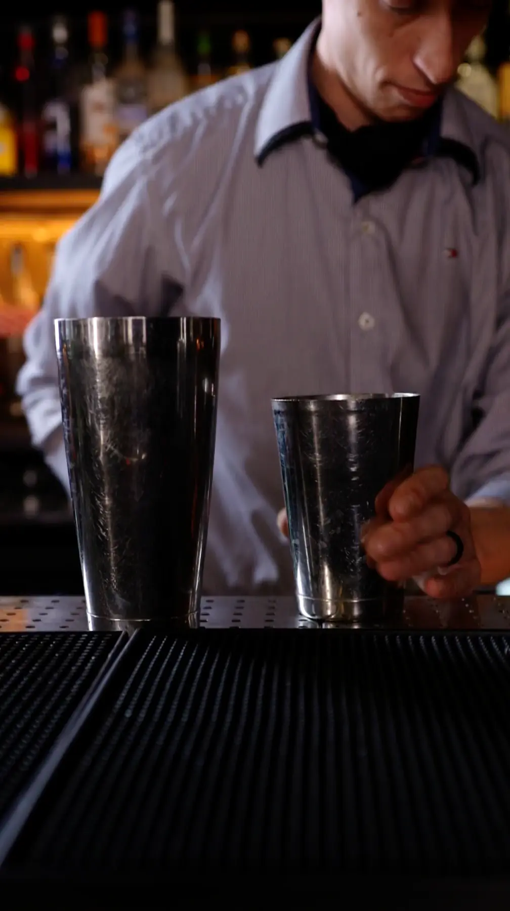 A man making a cocktail at a bar with two metal cups