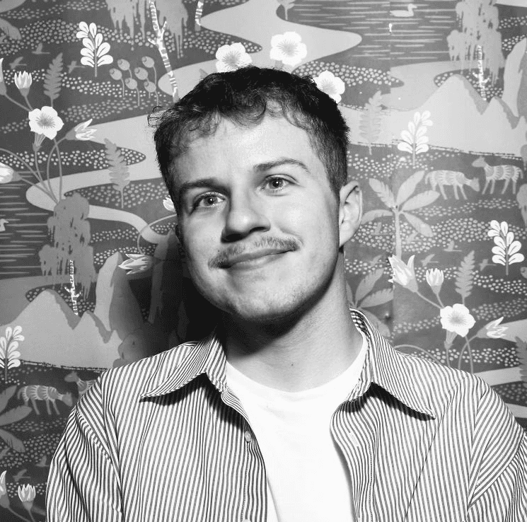 A thoughtful young person with dark hair gazes to the side, captured in soft black and white lighting.
