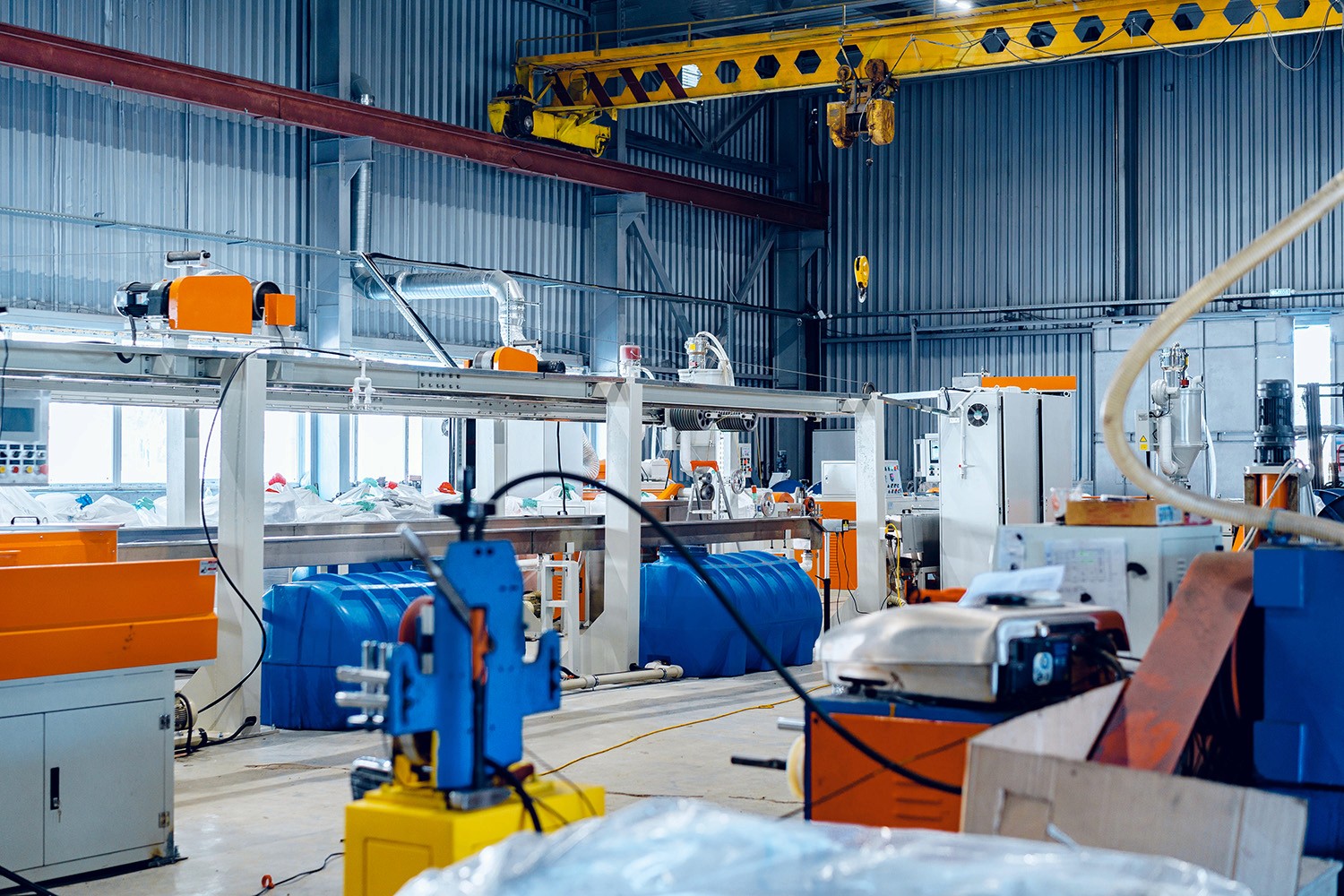 A modern industrial manufacturing facility with various machinery, blue storage tanks, and an overhead crane, filled with equipment for chemical production.