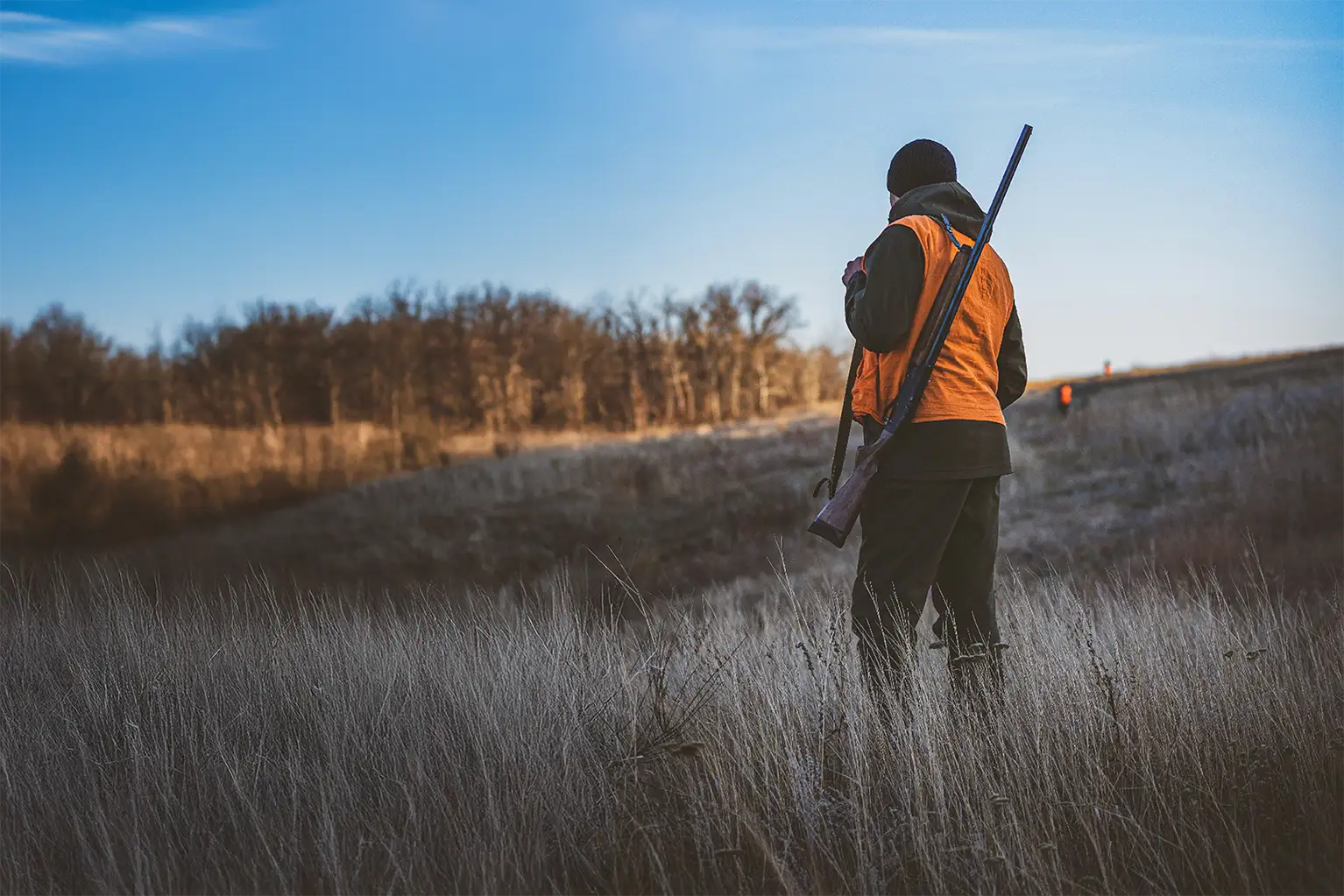 Jäger mit orangefarbener Warnweste bei einer Bewegungsjagd in offener Landschaft