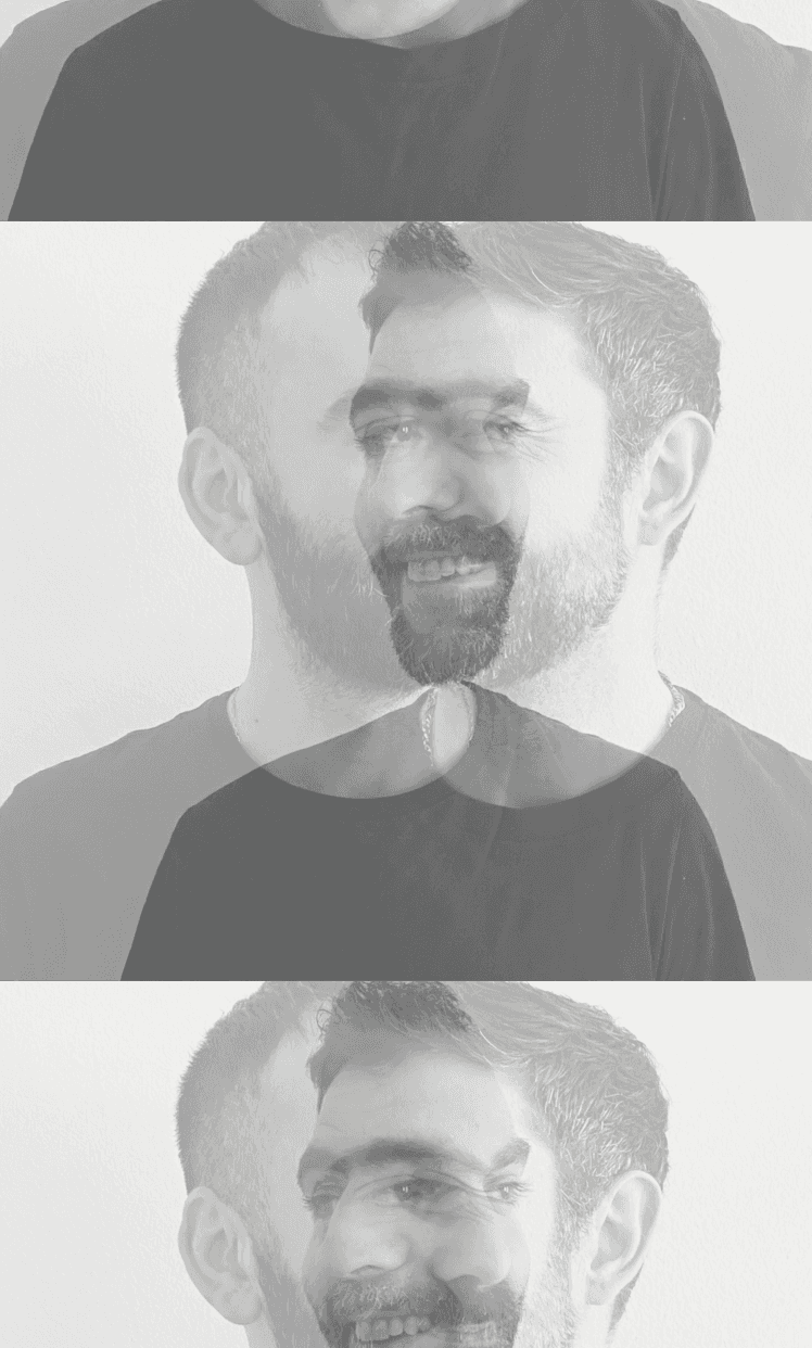 Close-up portrait of a person wearing a gray insulated hooded jacket with the hood up, showing their face framed by the hood against a light background.