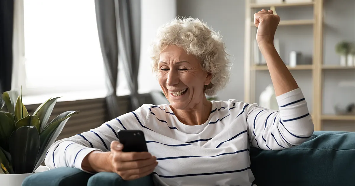 Glad kvinne deltar i Telekirken via sin telefon.