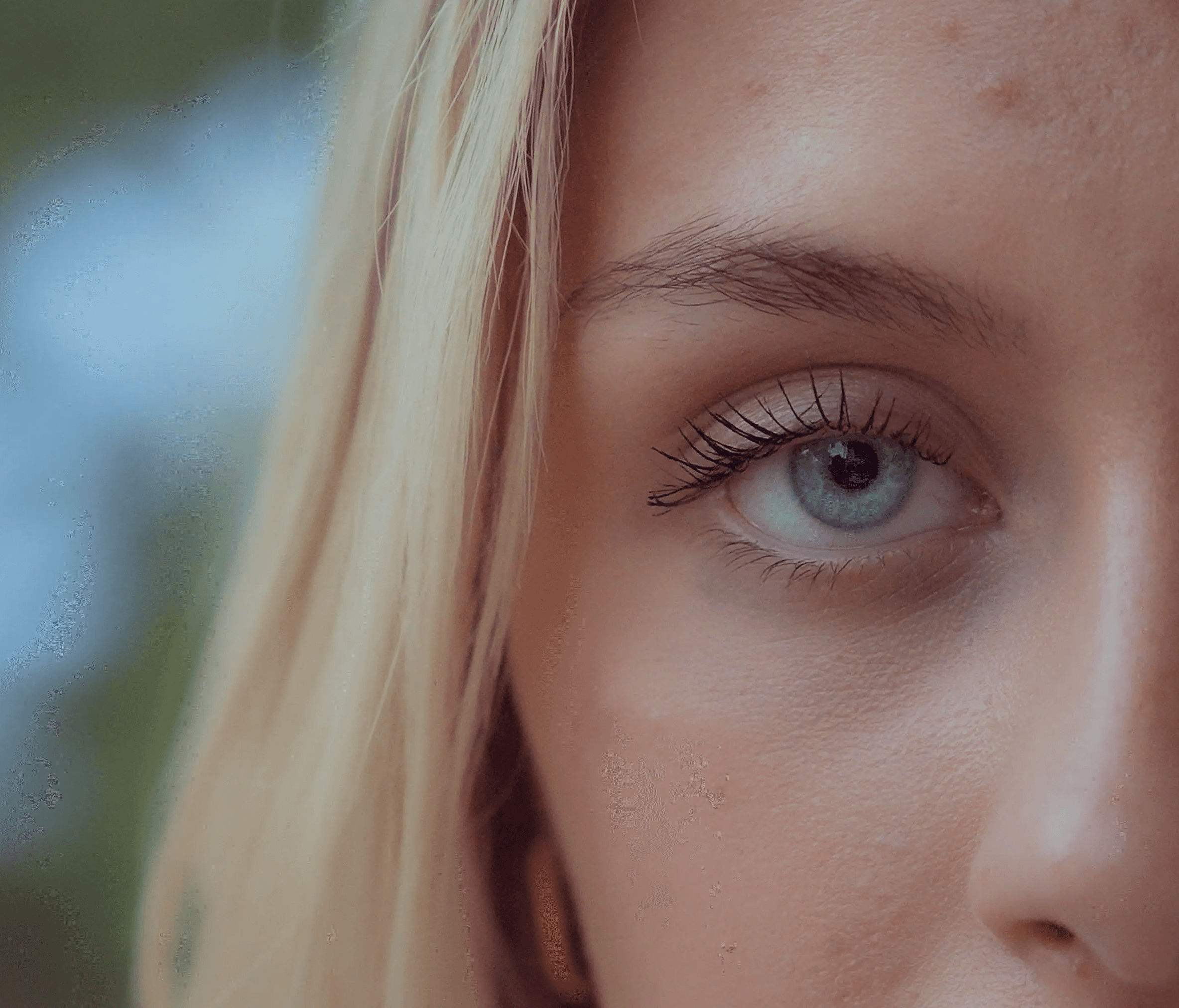 Close-up of a woman's face, focusing on one eye, with soft lighting and a blurred background.