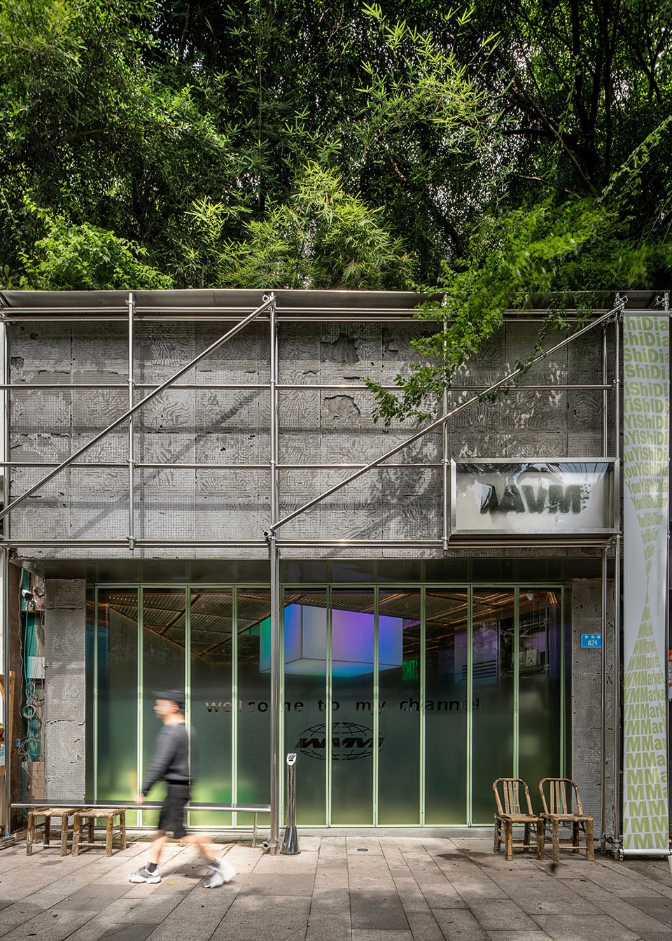 A small architectural tea house facade made of concrete and glass, featuring playful graphic elements on the walls, surrounded by green trees in an urban setting.