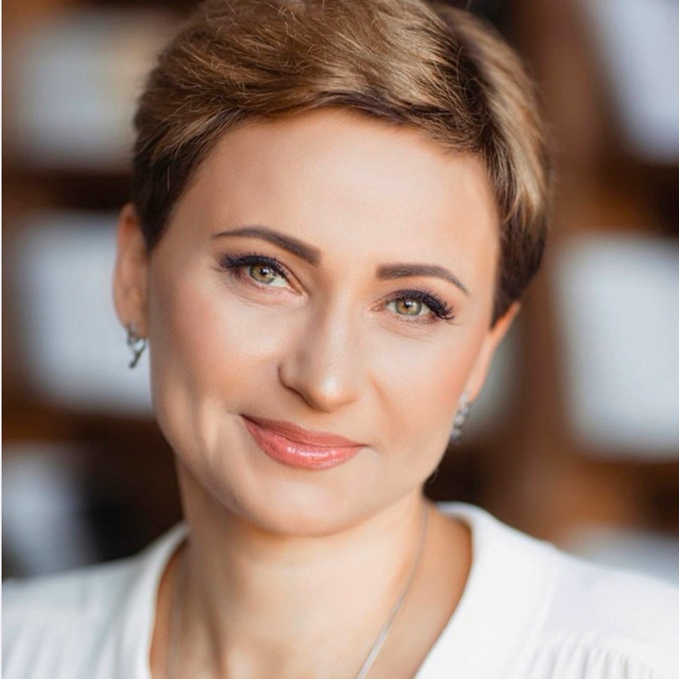 Black-and-white portrait of a man with an afro in motion, wearing a hoop earring and chain necklace, against a light gray background.