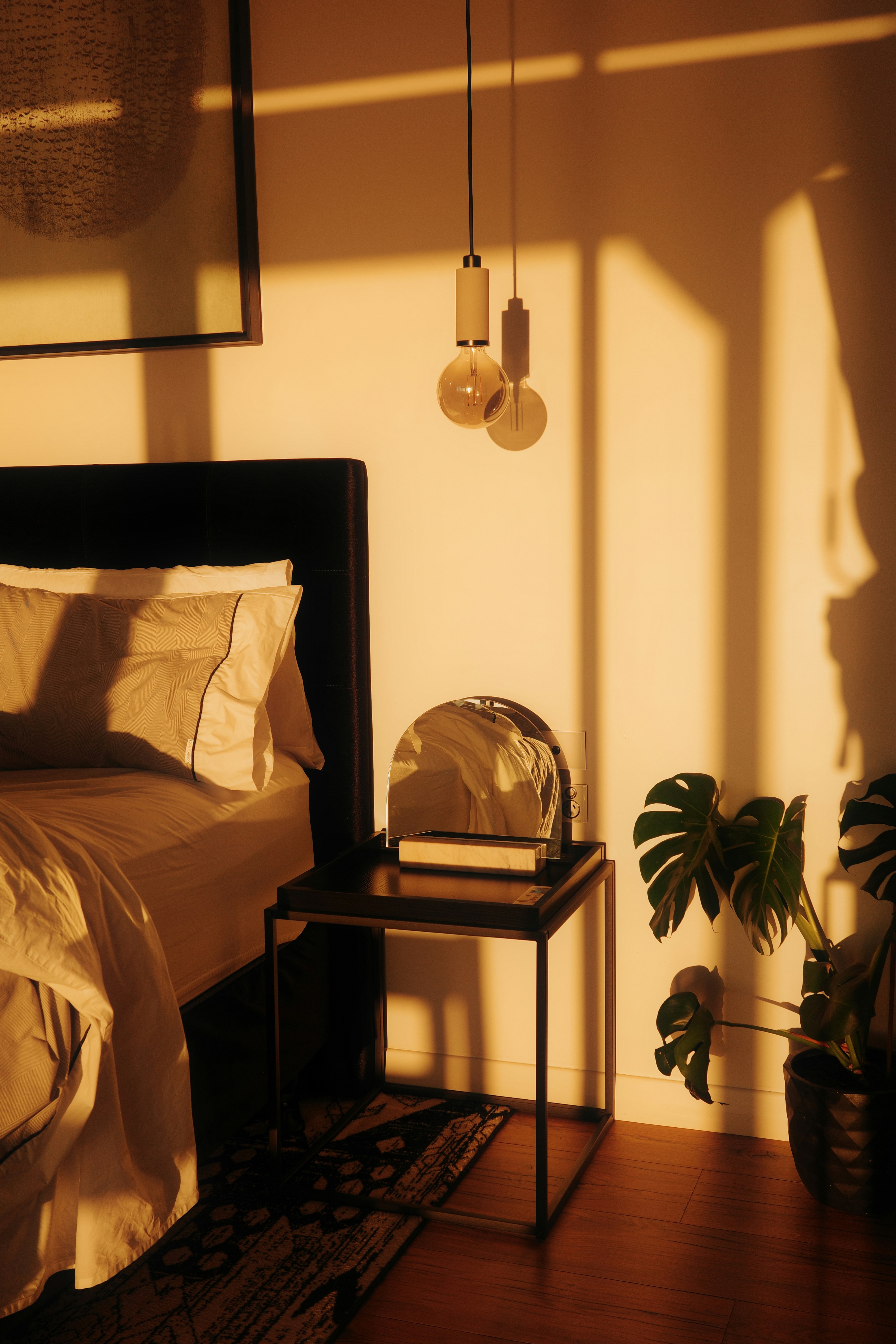 Warm light illuminates a bedroom with a bed and plant.