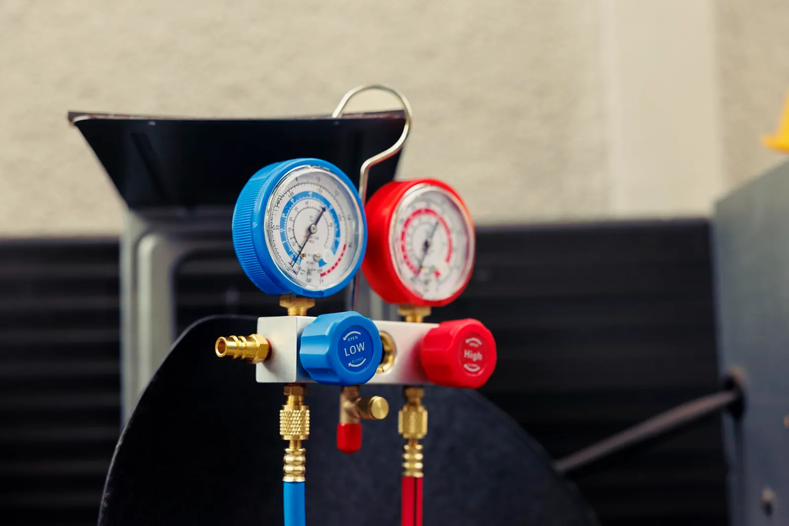 Red and blue HVAC manifold pressure gauges used for air conditioner problem diagnosis and refrigerant testing.