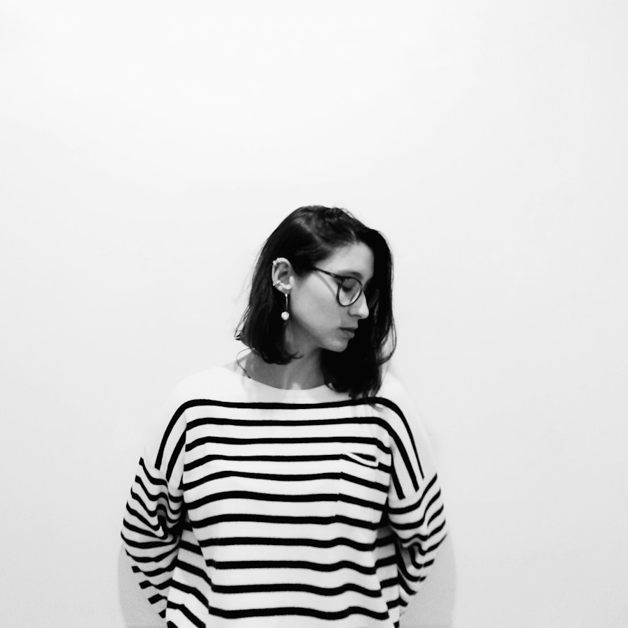 Woman in a striped Breton knit and round glasses against a white wall