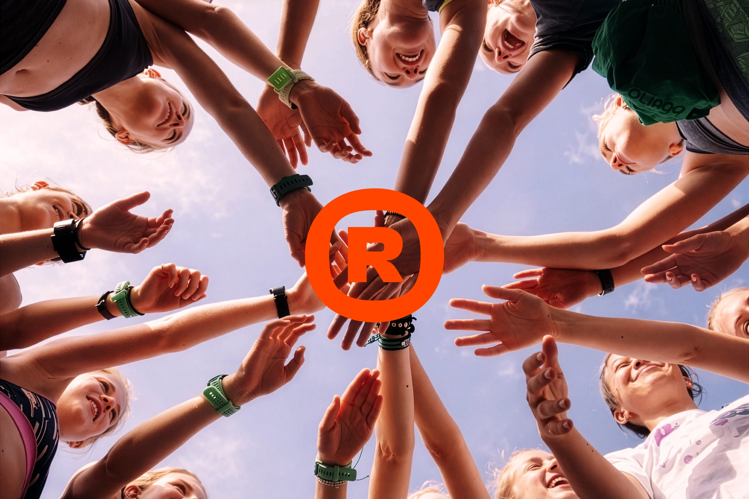 Smiling group's hands reach together, R logo in center, viewed from below.