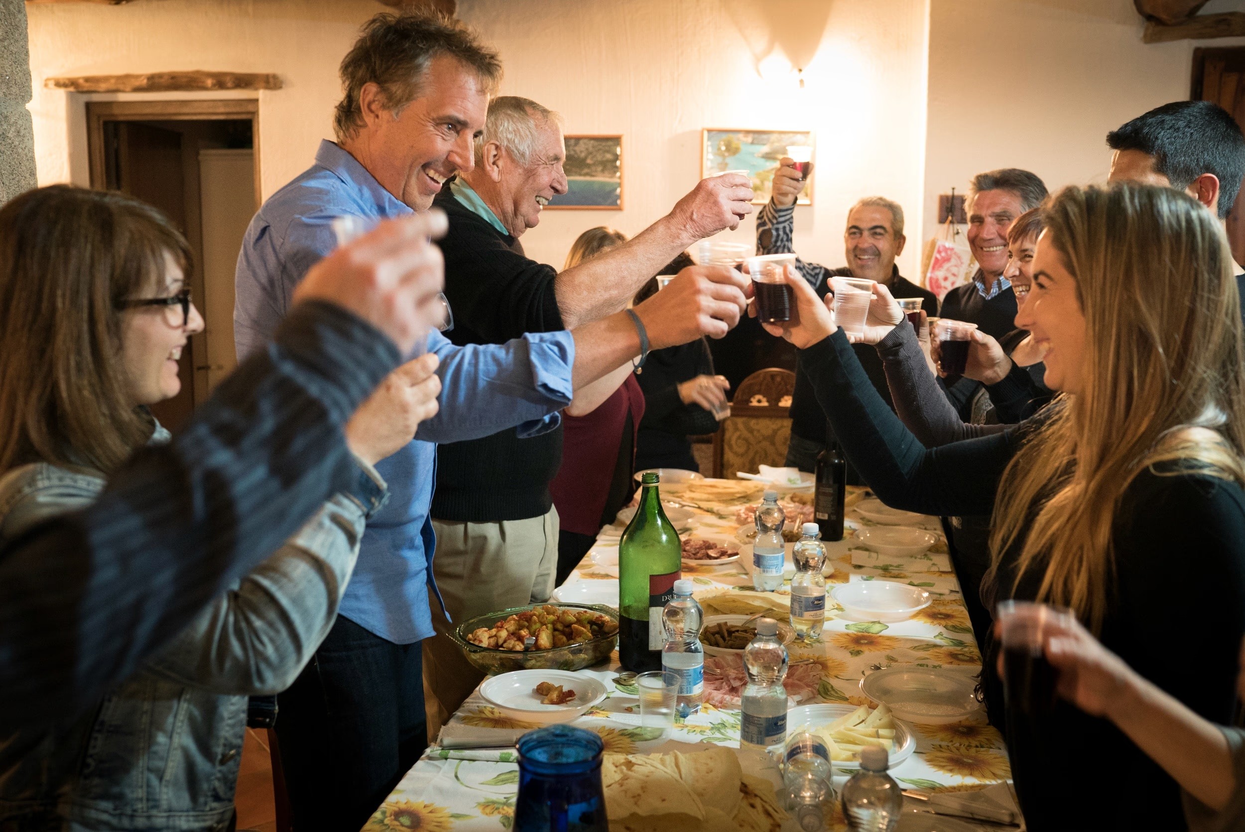 Group of people raising glasses in a toast around a long dinner table filled with food.