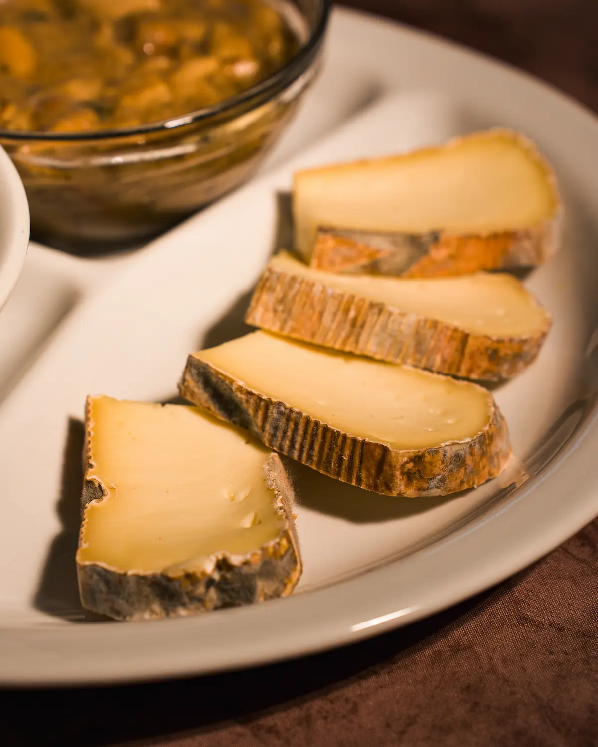 Four people dressed in light clothing walk along a vineyard path towards an old stone farmhouse, with lush grapevines on either side under a soft, golden morning light, capturing the essence of a serene countryside landscape.