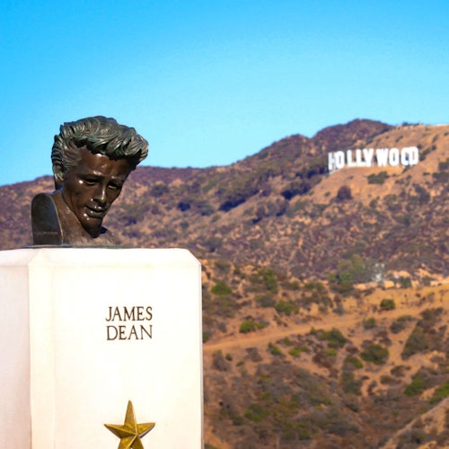 Bust of James Dean on a pedestal inscribed with his name, with the Hollywood sign in the background.