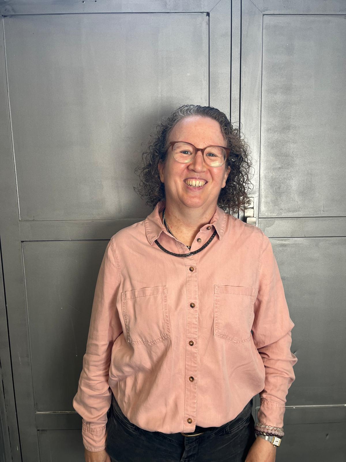 A smiling women in a pik shirt standing in front of a grey background