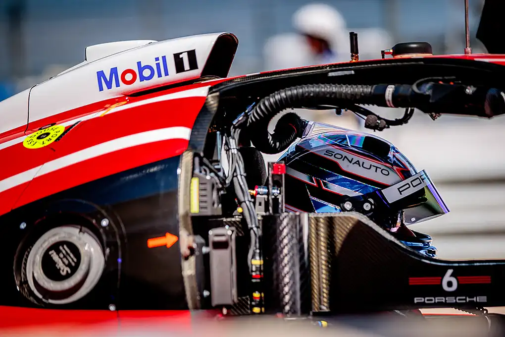 Close-up of a red, white, and black Porsche race car with a visible driver inside and a Mobil 1 logo prominently displayed on the roof.