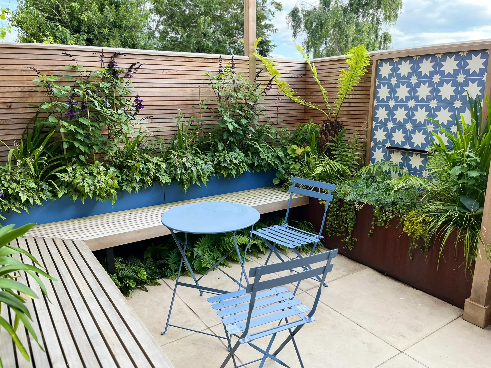 A serene garden space features a small table and chairs surrounded by lush greenery and decorative plants.