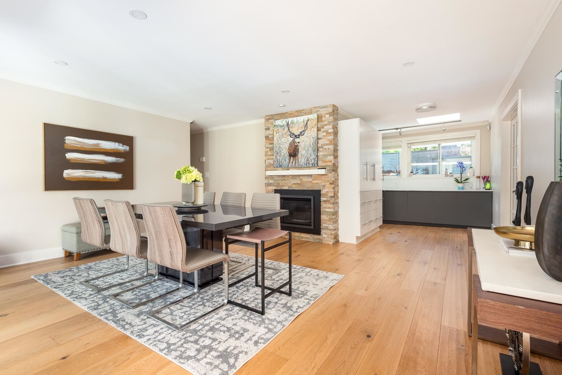 Bright living room with hardwood floors, a dining table, artwork, and a cozy fireplace. Natural light floods the space.